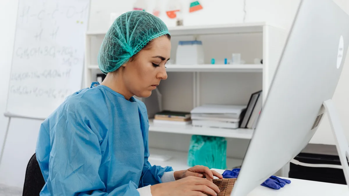 A female healthcare professional in scrub suit working on a computer in a laboratory setting.