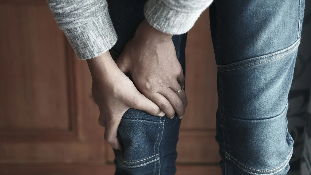 A person holds their knee in denim jeans, showing a sense of tension.