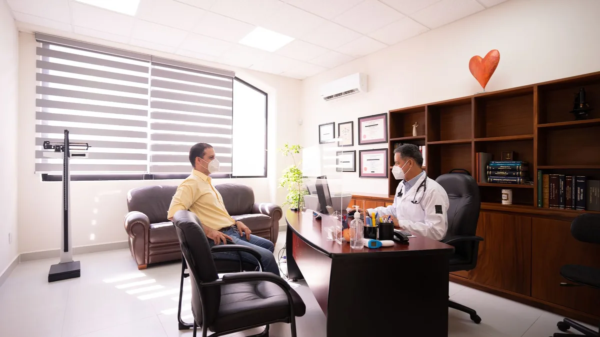 A patient consults with a masked doctor in a well-lit, modern office.