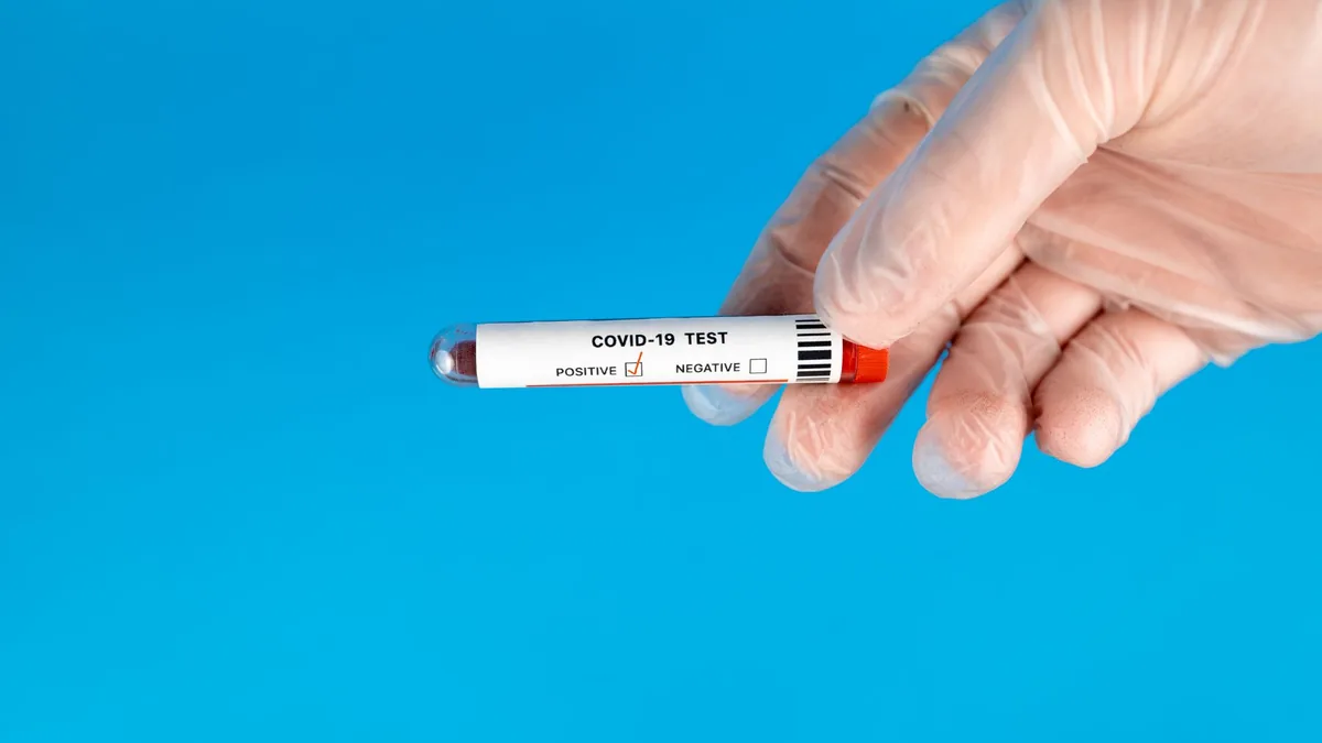 Gloved hand holding COVID-19 test tube with blood sample against blue background.
