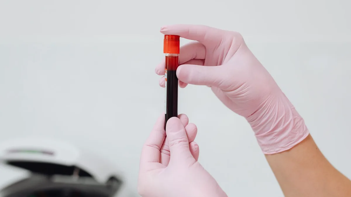 Close-up of gloved hands holding a blood sample in a test tube.