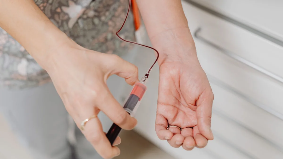A close-up view of a blood draw procedure with syringe and vial, focusing on healthcare treatment.