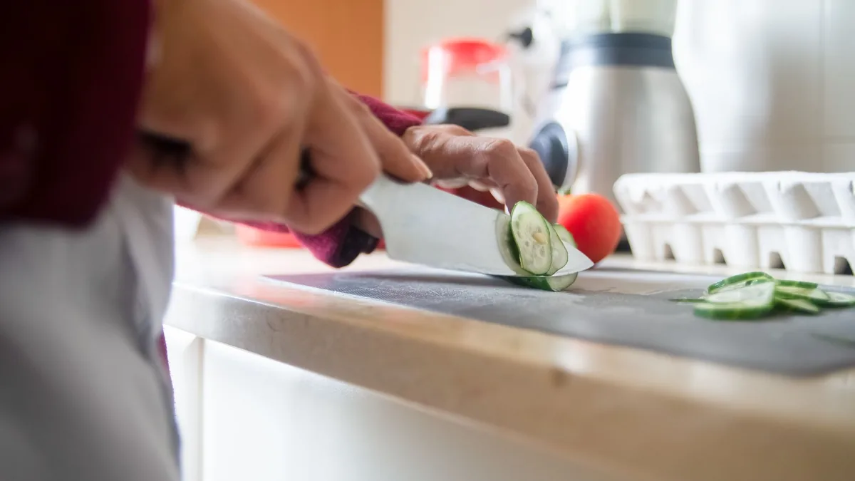 Close-up of a person slicing cucumbers on a kitchen counter for a healthy meal prep.