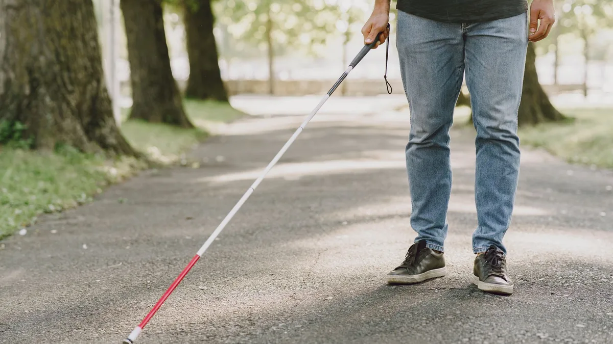 An adult man walking on a park path with a white cane.