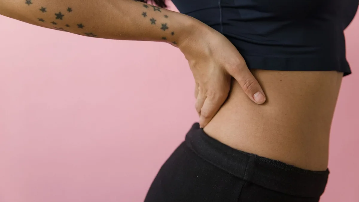 Side view of a tattooed hand on hip against a pink background in a studio setting.
