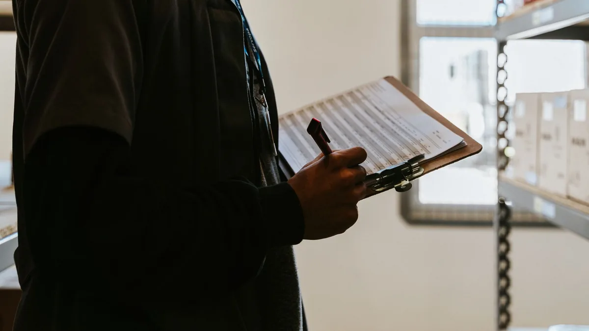Industrial worker managing inventory in a warehouse with a clipboard and checklist.
