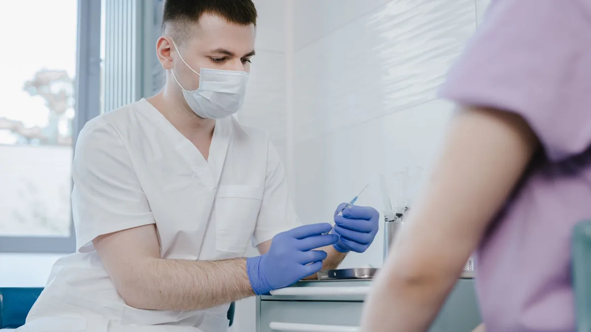 Healthcare worker in protective gear preparing a syringe for vaccination indoors.