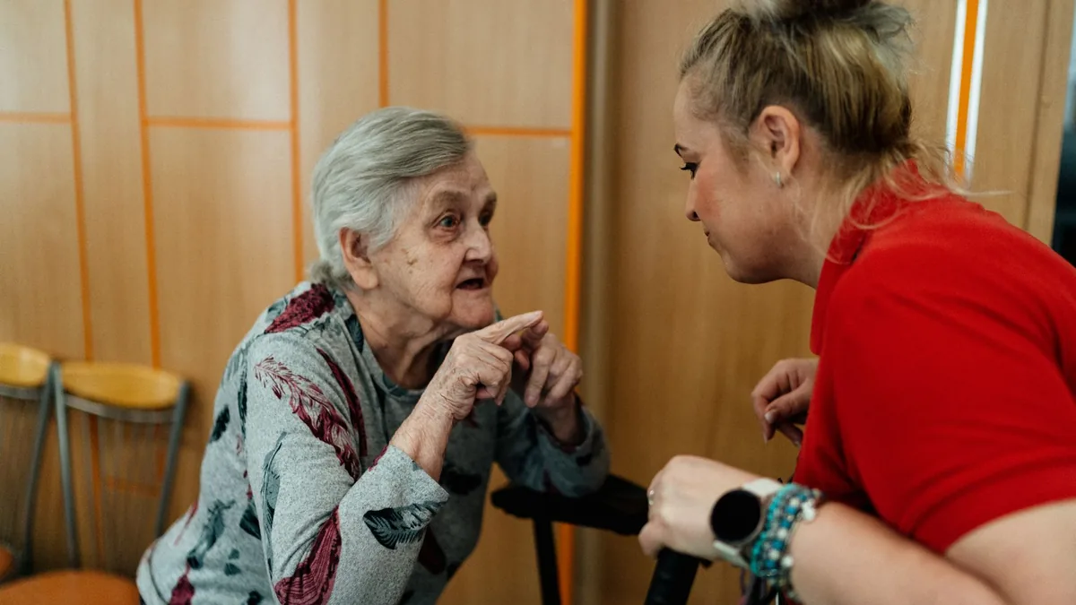 Elderly woman and caregiver in conversation inside a room in Karviná, Česko.