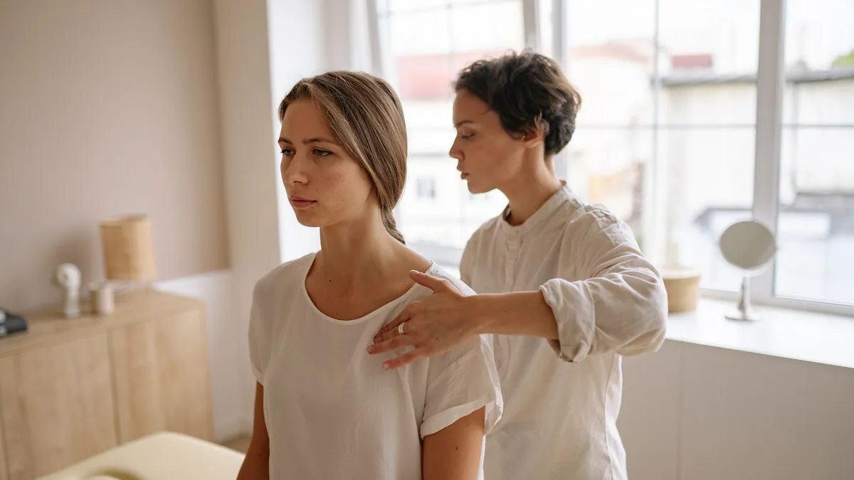 A woman receives shoulder therapy from a therapist in a serene room with natural light.