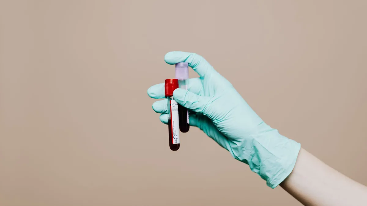 Close-up of a gloved hand holding blood test tubes against neutral background.