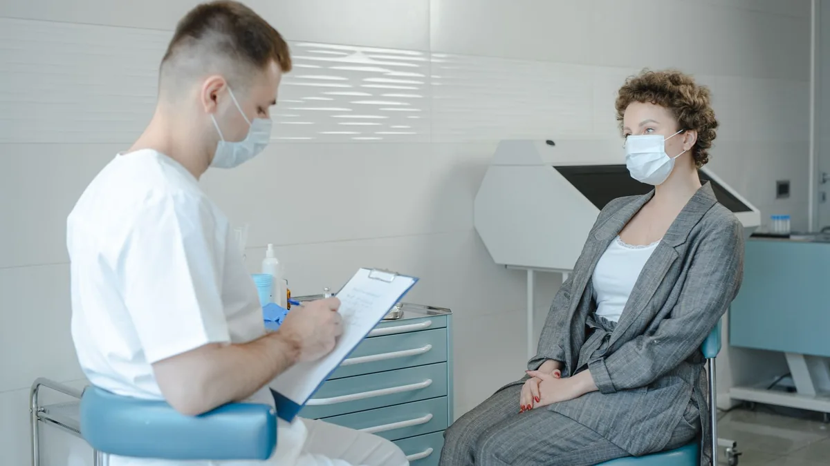 A doctor in a face mask consults a patient in a clinic, reflecting the new normal.