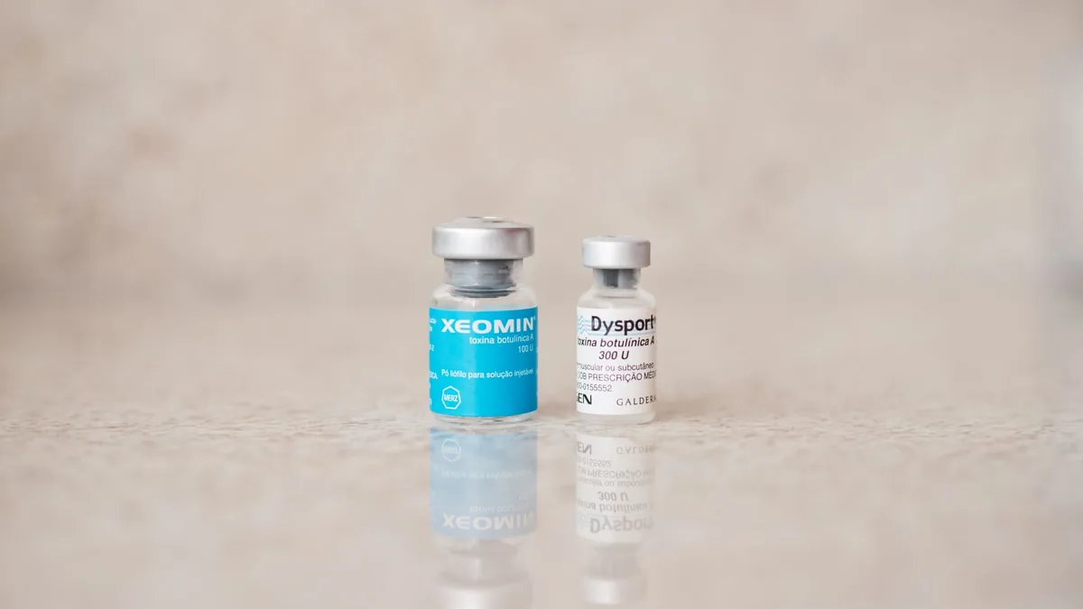 Close-up of Xeomin and Dysport bottles reflecting on a surface, shot indoors.