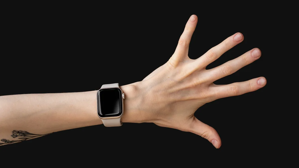 Elegant hand wearing a smartwatch with a tattooed wrist against a dark studio backdrop.