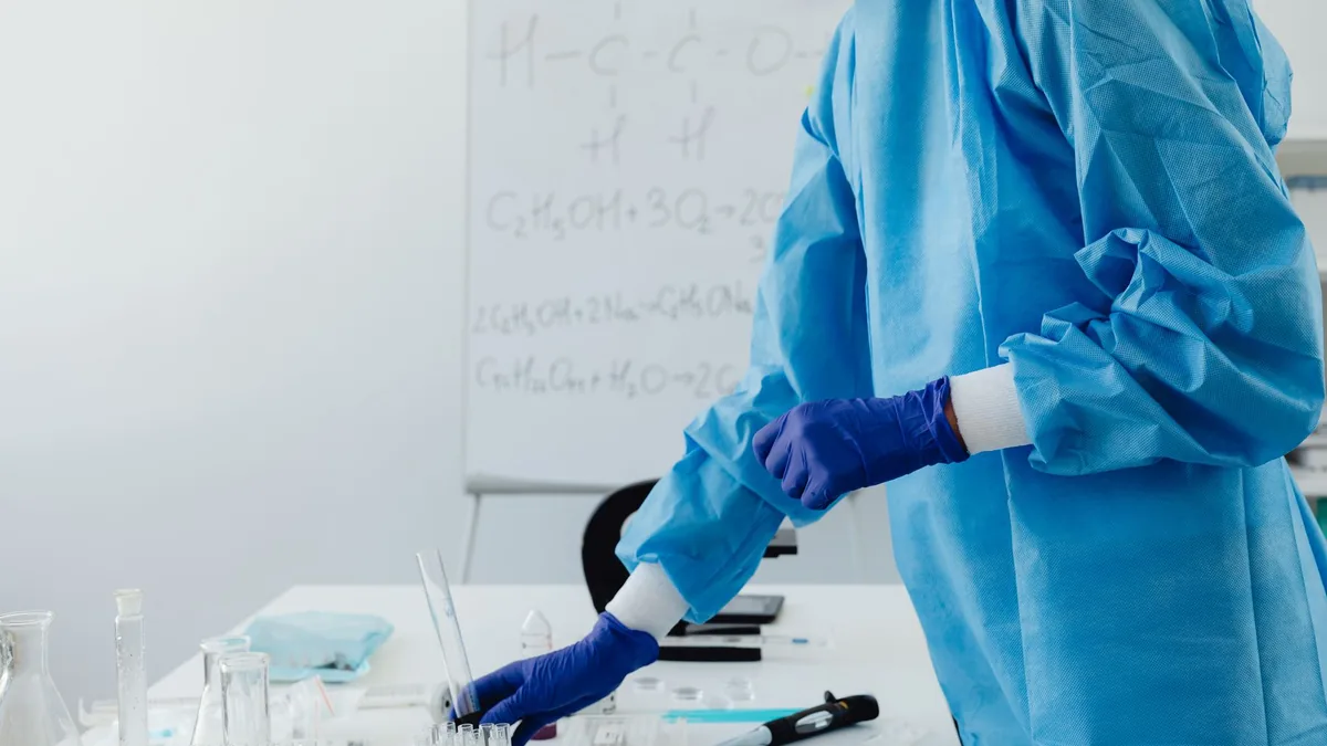 Scientist in protective clothing working in lab with chemical formulas on whiteboard.