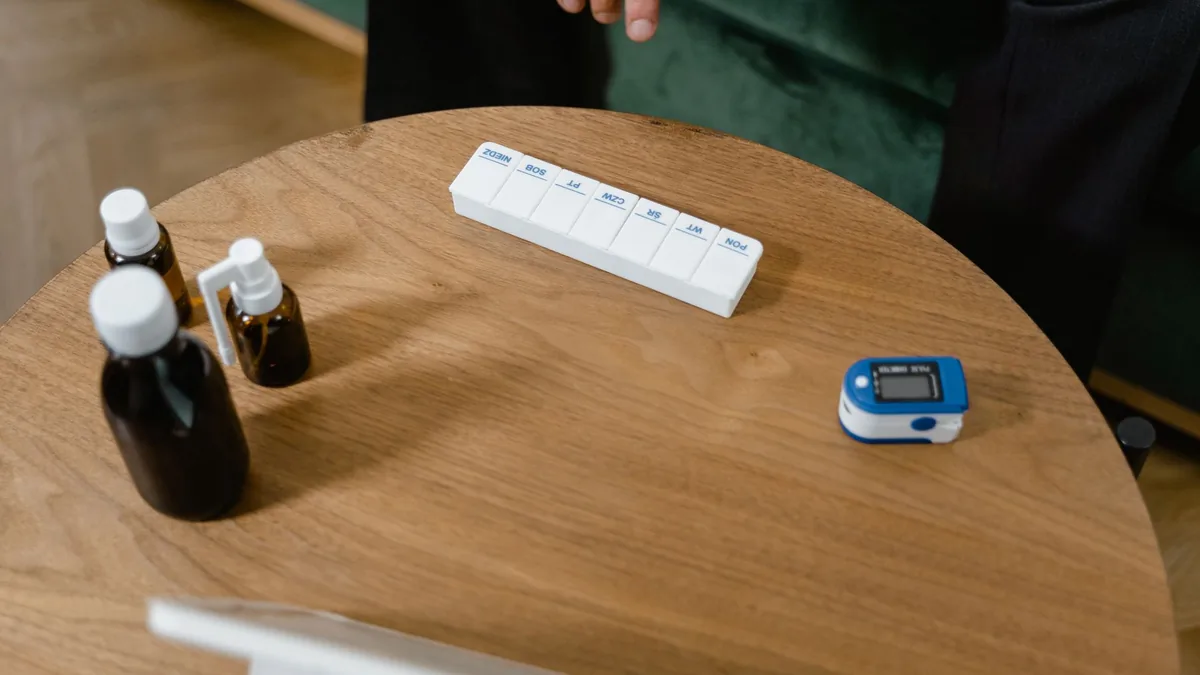 Pill organizer and medication bottles on a wooden table with a pulse oximeter.