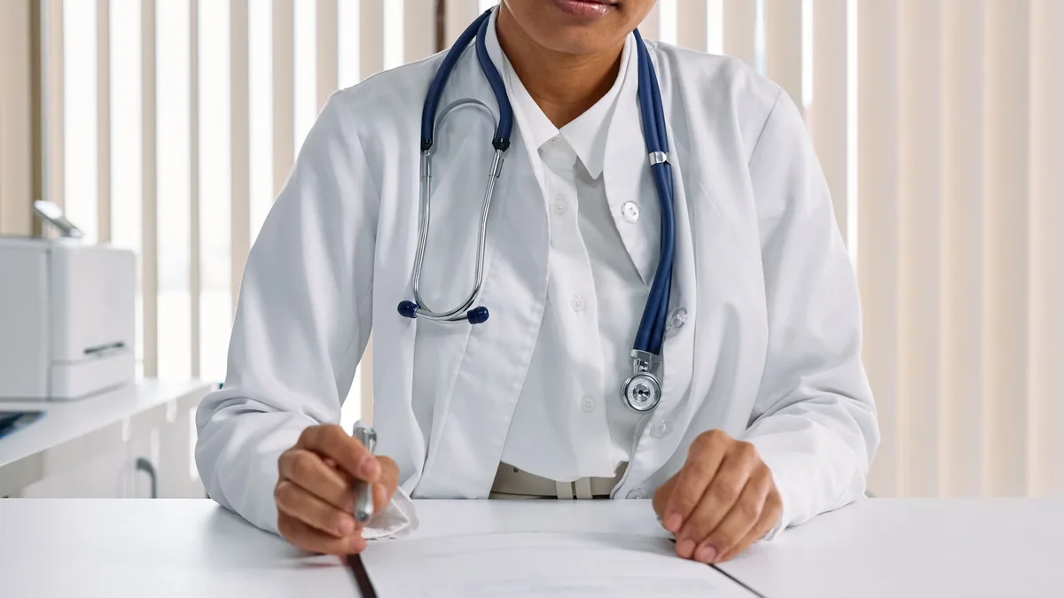 A focused doctor with stethoscope recording patient details in an office setting.