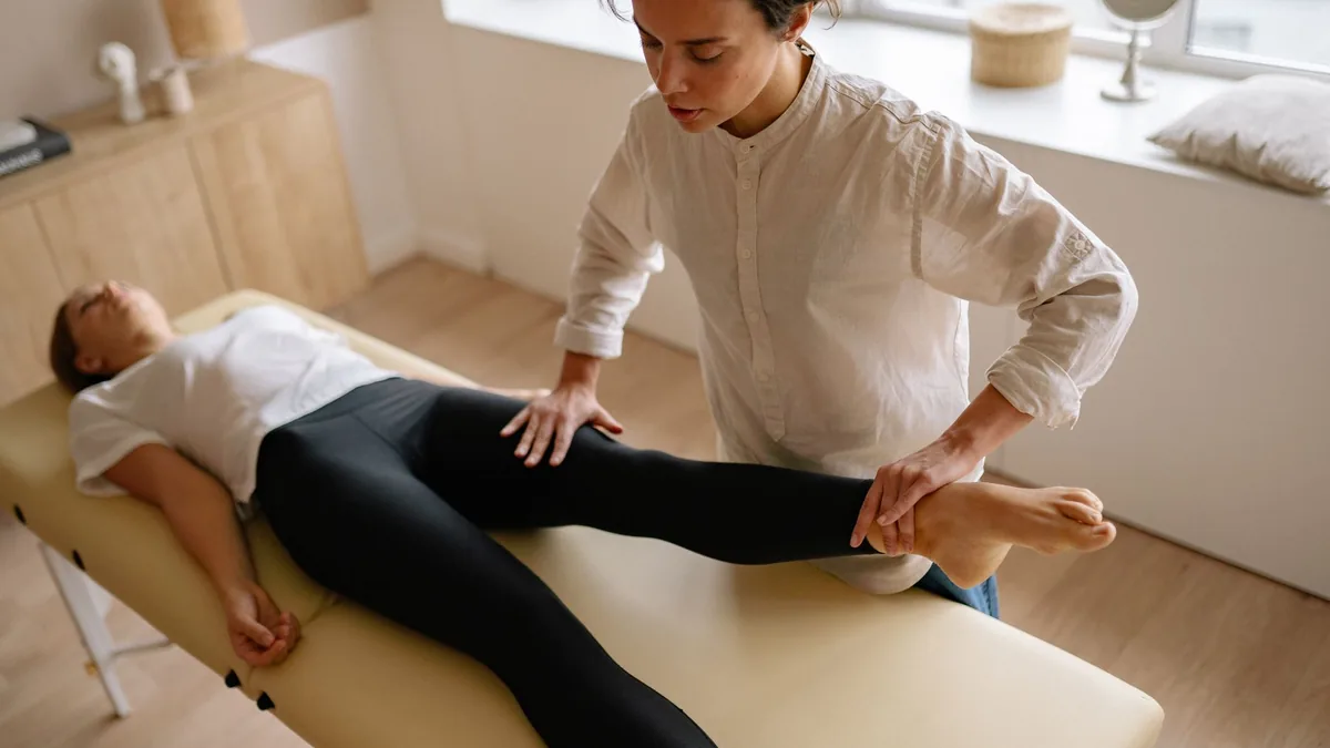 A physiotherapist assists a woman with leg rehabilitation therapy in a calm treatment room.
