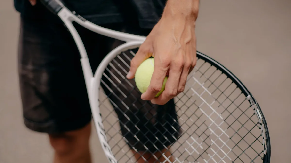 Detailed view of a tennis player holding a tennis ball and racket, preparing for a serve.