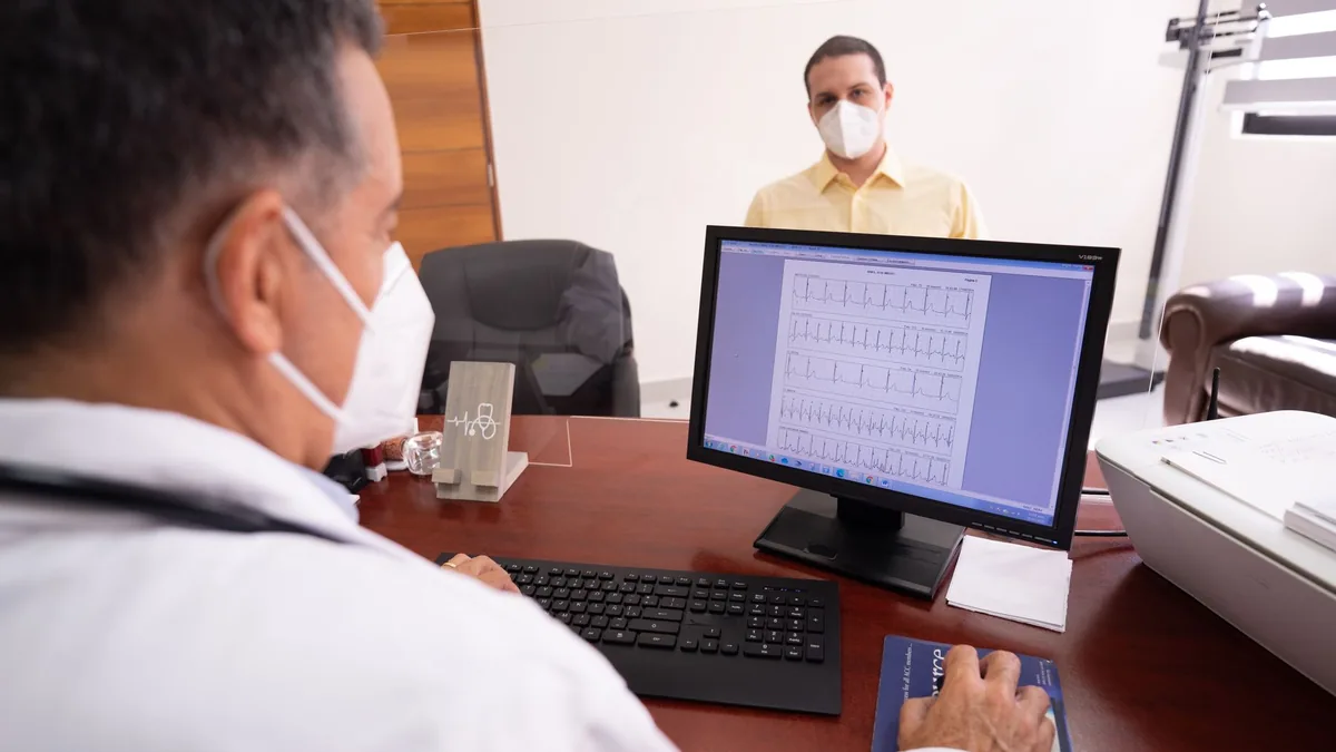 Doctor consults patient remotely using computer and face masks for safety.