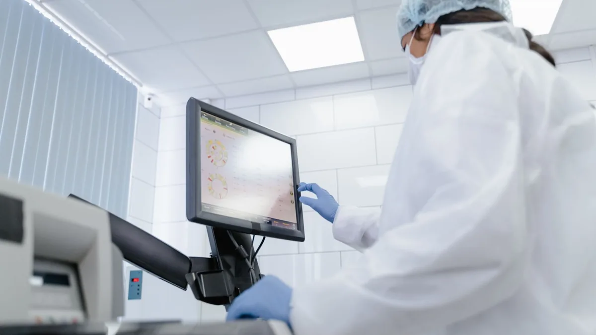 Woman in lab coat using touchscreen monitor in a modern laboratory setting.