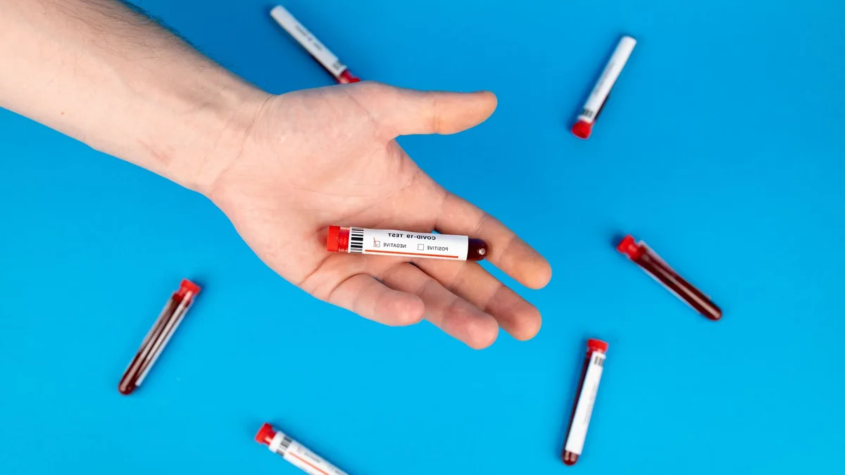 Close-up of a hand holding a blood sample vial on blue background.