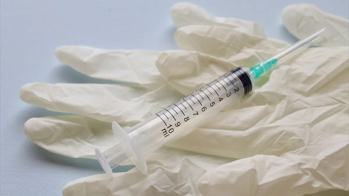 Close-up of a syringe and medical gloves on a flat surface.
