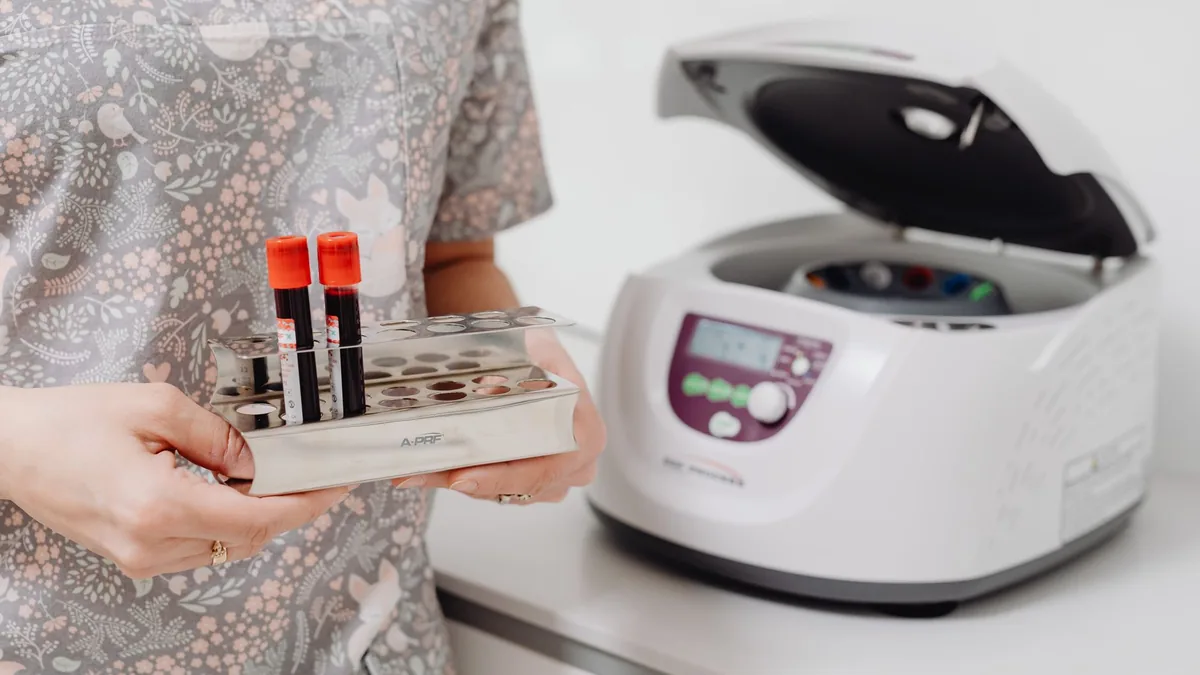 Healthcare professional holding blood vials next to a laboratory centrifuge, indoors.