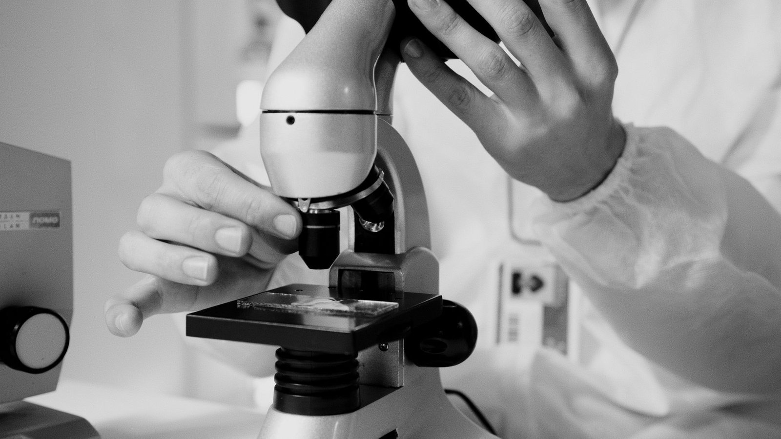 A researcher adjusting a microscope objective over a prepared tissue slide, photographed in black and white