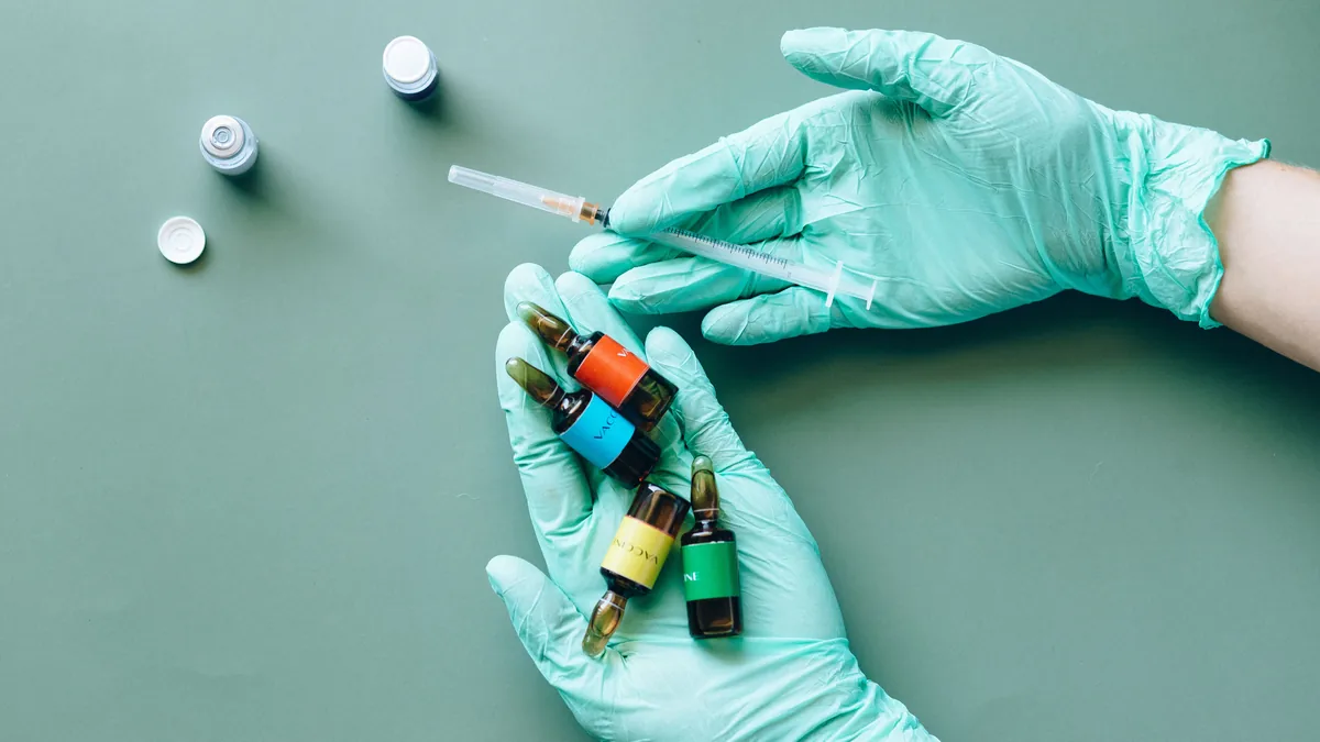 Gloved hands holding small medication ampules beside a syringe