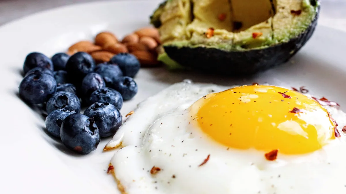 Fried egg, half an avocado, blueberries and almonds on a white plate