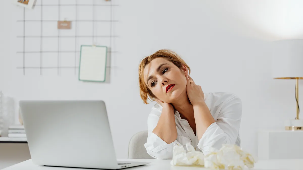 Tired woman at her desk holding the back of her aching neck