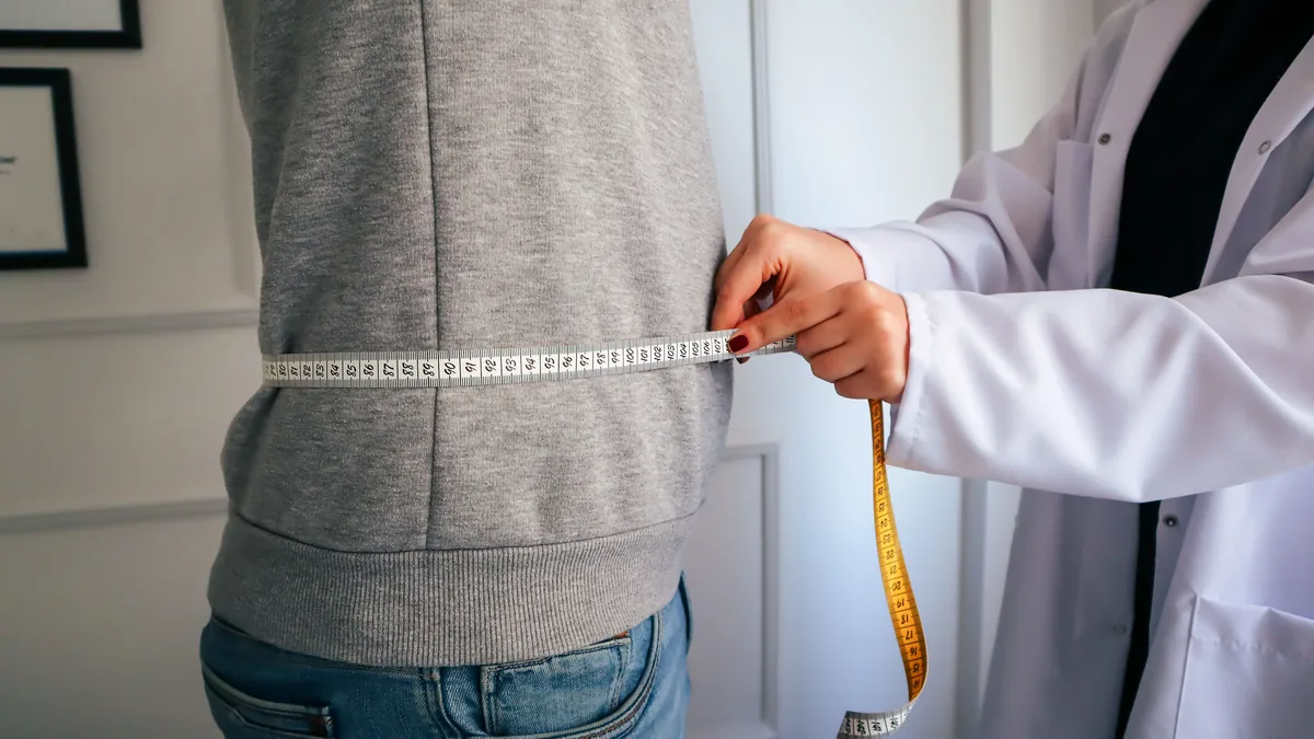 Clinician measuring a patient's waist with a tape measure to assess metabolic health