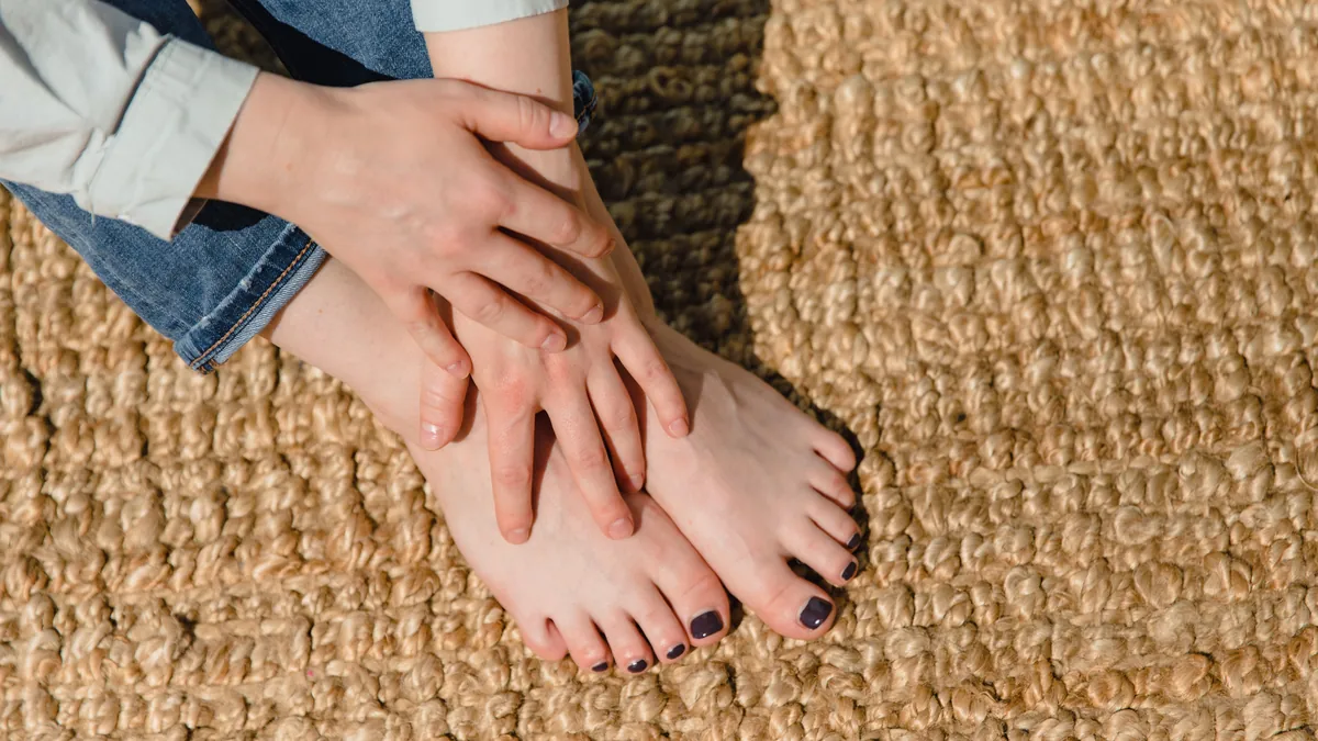 Woman seated on a woven rug holding her bare foot with both hands