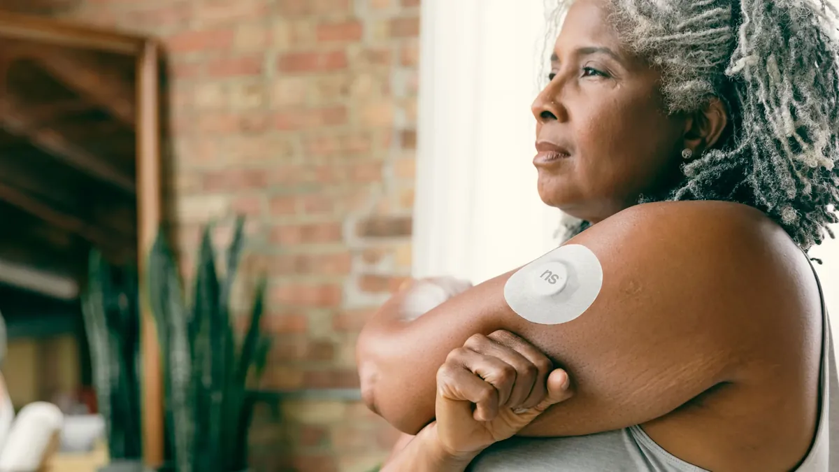 Older woman wearing a continuous glucose monitor sensor on the back of her upper arm