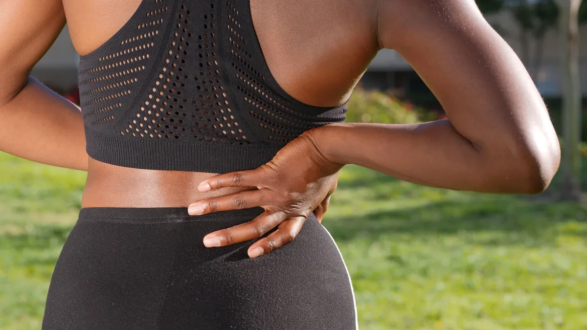 Woman holding her lower back where facet joint arthritis often causes spinal pain