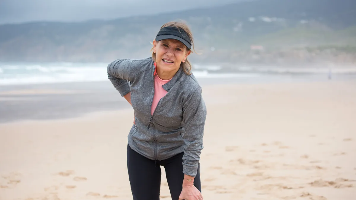 Older woman on a walk pausing in pain with a hand pressed to her hip