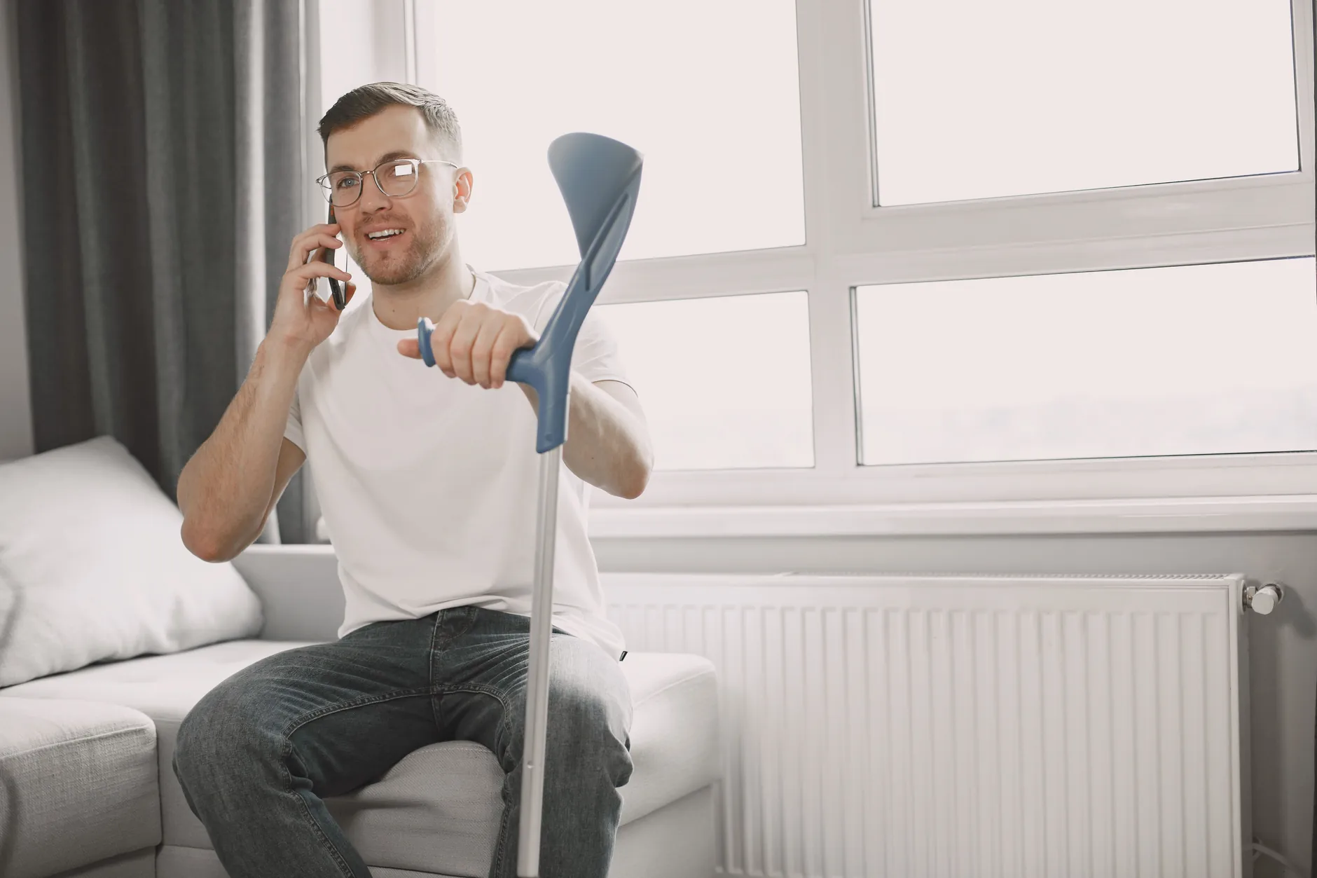 Man recovering from a leg injury sitting on a couch at home with a forearm crutch