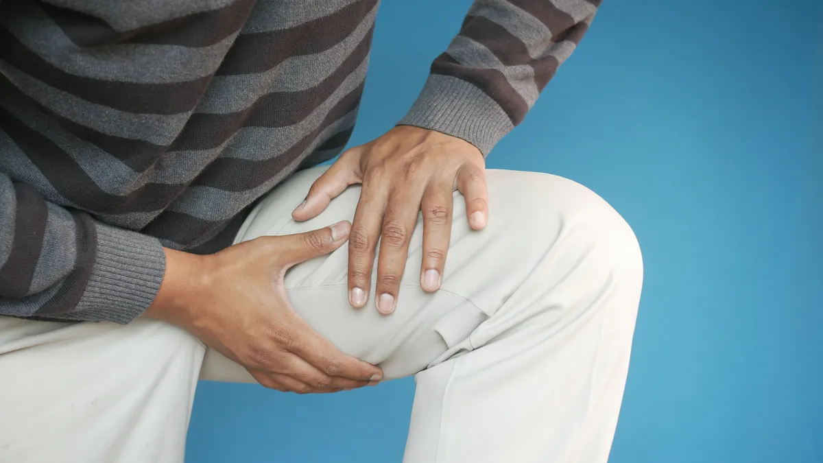 Man in a striped sweater holding his knee with both hands