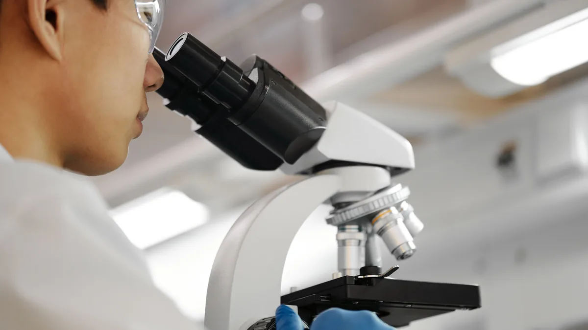 Researcher examining cell samples under a microscope to study mitochondrial function