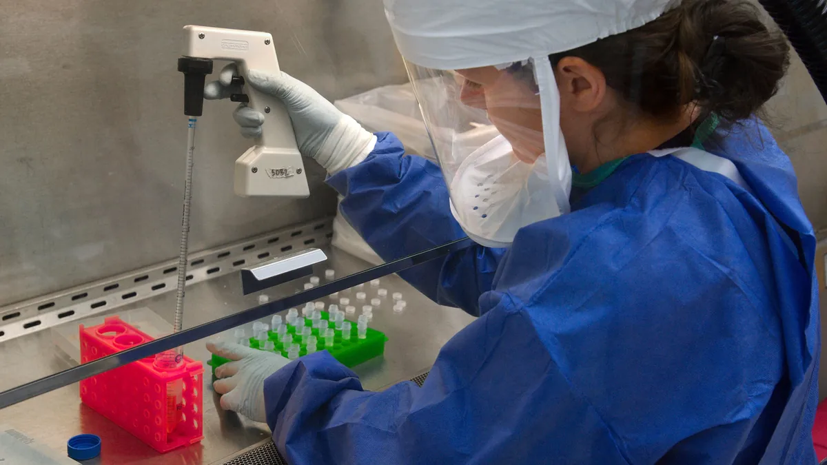 Technician in gown, gloves and face shield working inside a sterile biosafety cabinet