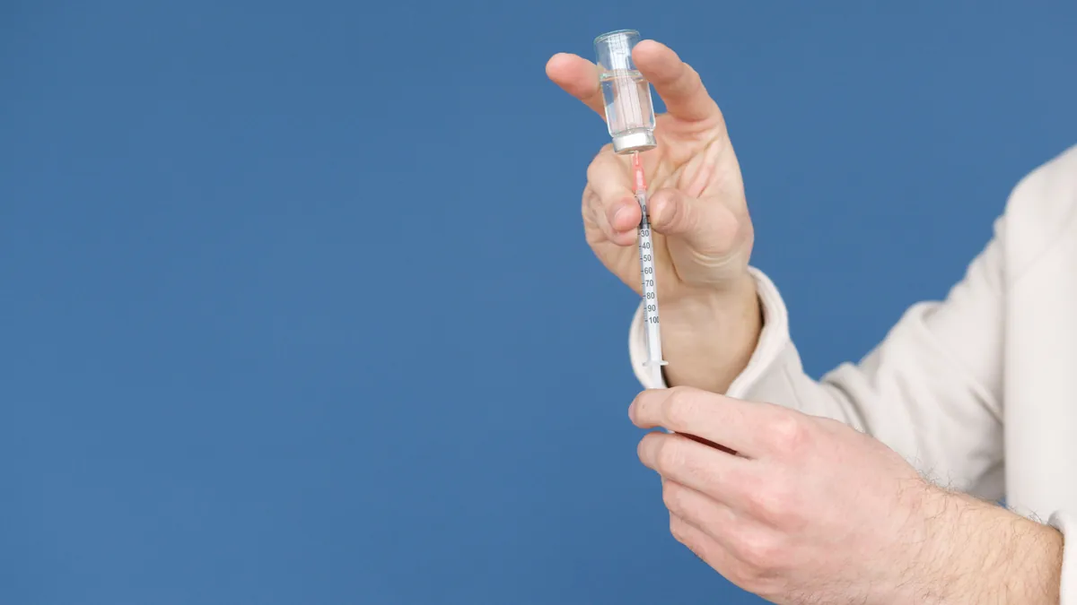 Hands drawing medication from a small vial into a syringe