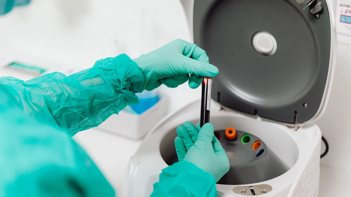 Gloved lab technician loading blood tubes into a centrifuge to separate platelets