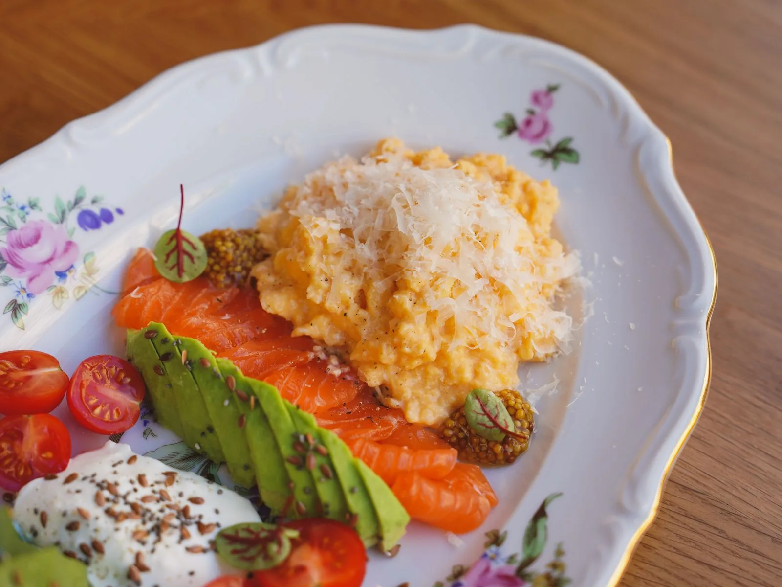 Plate of scrambled eggs, smoked salmon, sliced avocado, cherry tomatoes and yogurt, a whole-food low-carb meal