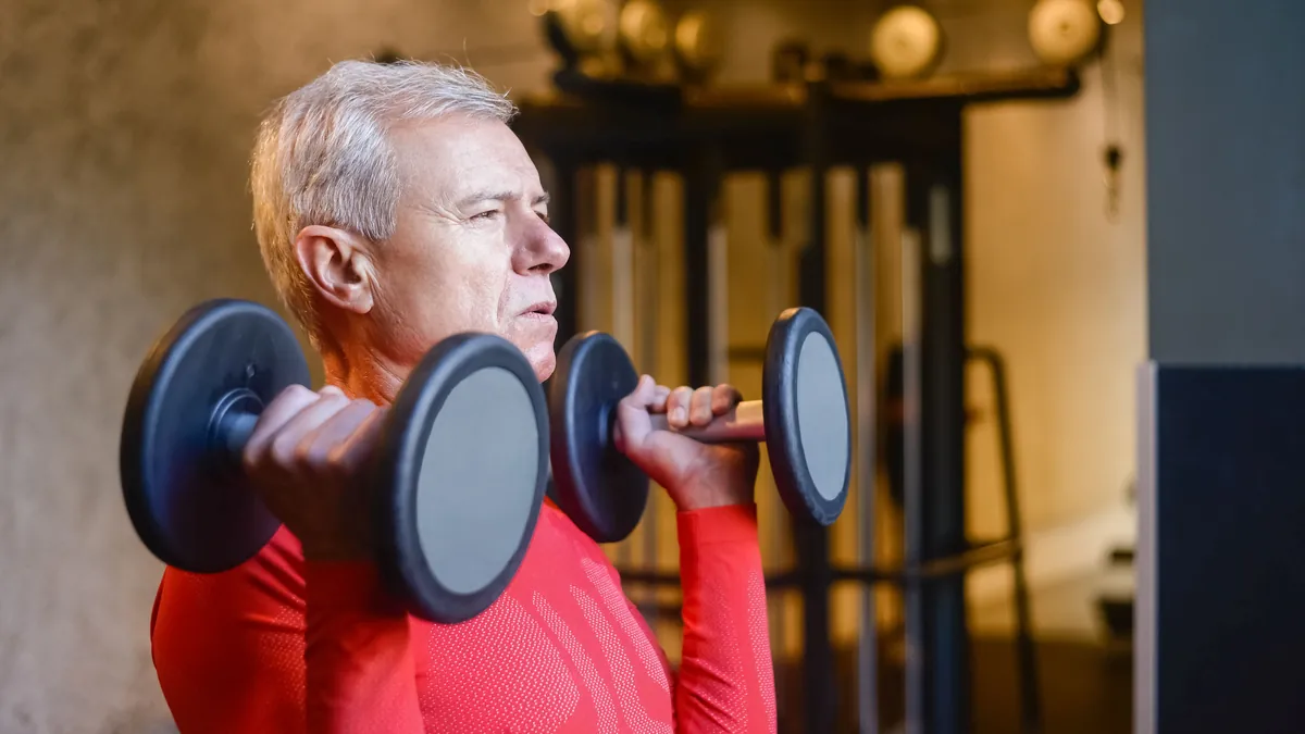 Older man lifting a pair of dumbbells in a gym to build muscle