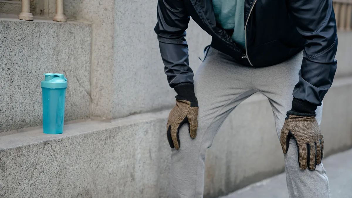 Active man pausing outdoors with both hands resting on his knees