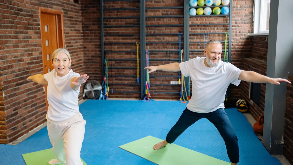 Older man and woman holding lunge poses on exercise mats in a gym